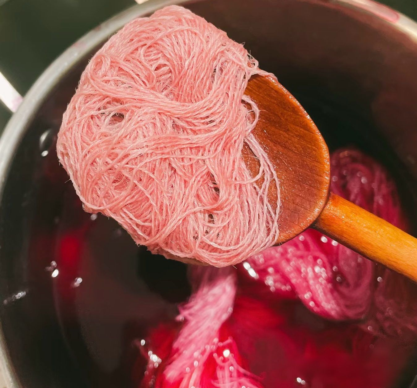 Hand-dyed pink wool yarn lifted from a natural dye bath on a wooden spoon