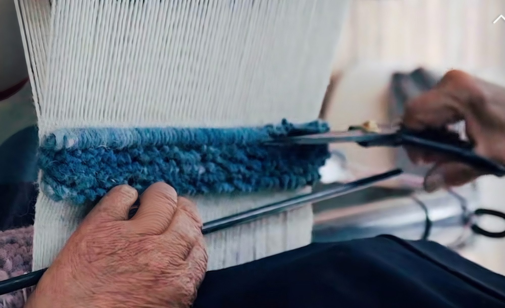 Artisan hands trimming indigo wool pile on a traditional loom